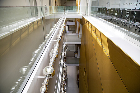 L’œuvre, alignement de vases, soupières, chopes, verres... argentés entre en dialogue avec la toile tendue dorée, face à elle. (© C.Schröder/Unistra)